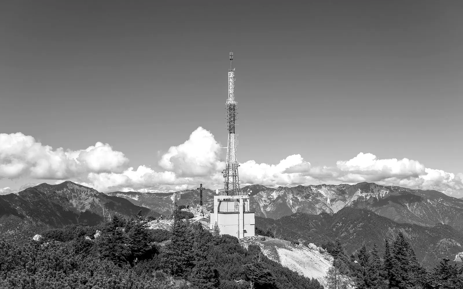 Torre de transmisión roja y blanca sobre una montaña con nubes